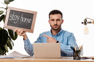 bearded freelancer pointing with finger at chalk board with stay home lettering isolated on white  clipart