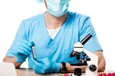 Tıbbi maskeli bir bilim adamının elinde Coronavirus harfleriyle beyaz üzerinde izole edilmiş mikroskop ile test tüpü tutarken görüntüsü. 