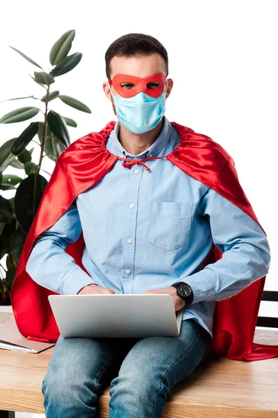 戴着医疗面罩 身穿超级英雄服装的自由职业者 使用笔记本电脑 坐在桌子上 与白人隔离 — 图库照片