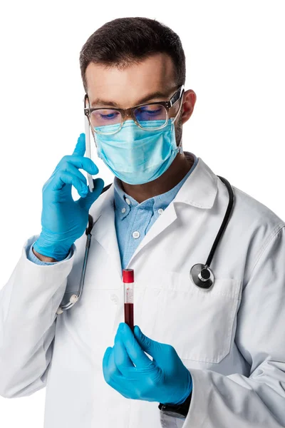 白人に単離された血液サンプルで検査管を保持しながらスマートフォンで話している医療用マスクや眼鏡の医師 — ストック写真
