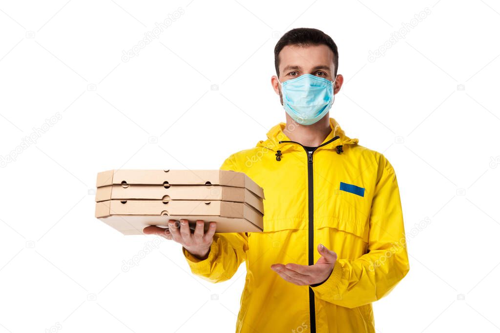 delivery man in medical mask pointing with hand at pizza boxes isolated on white 