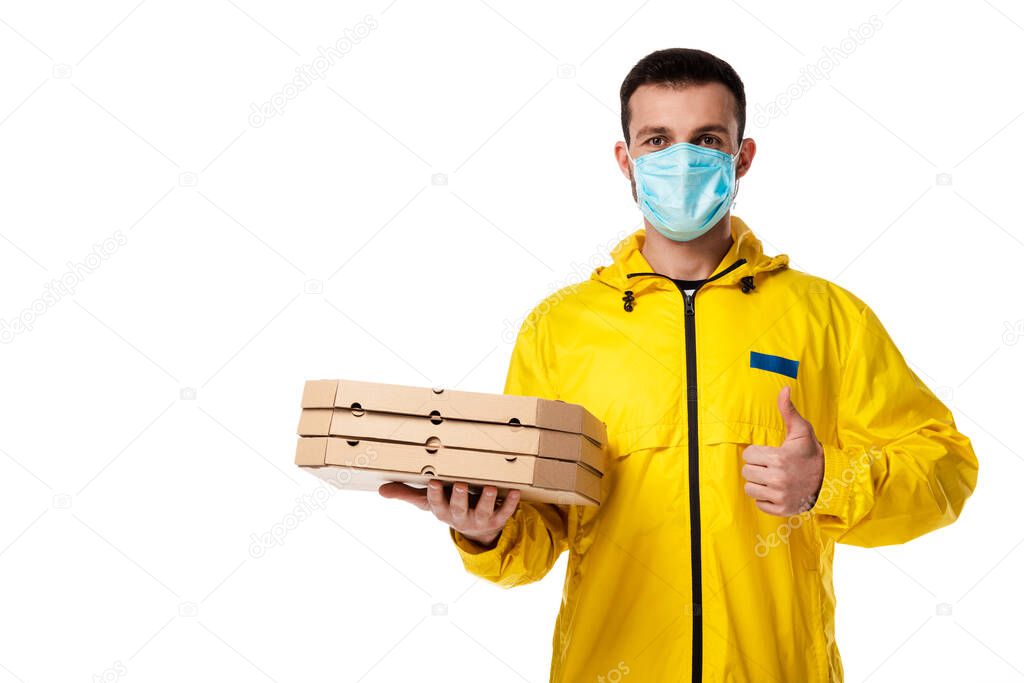 delivery man in medical mask holding pizza boxes and showing thumb up isolated on white 
