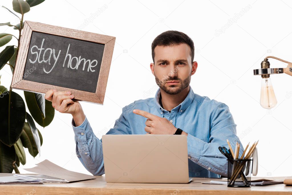 bearded freelancer pointing with finger at chalk board with stay home lettering isolated on white 