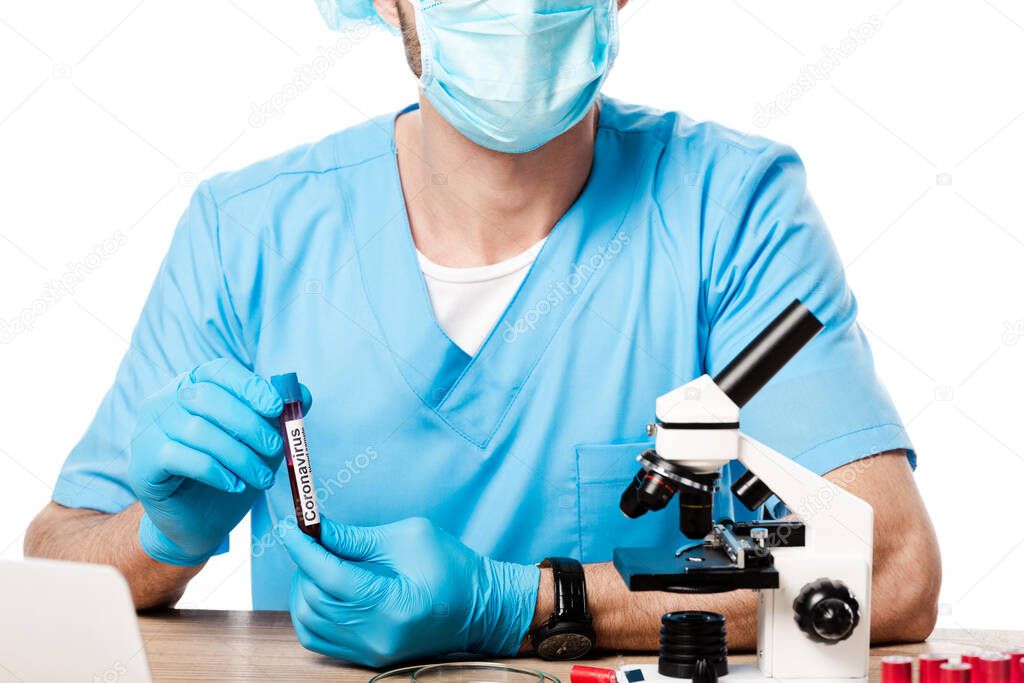 cropped view of scientist in medical mask holding test tube with coronavirus lettering near microscope isolated on white 
