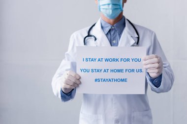Orta yaşlı, lateks eldivenli bir doktor. Plaket tutuyor. Ben senin için çalışıyorum, sen evde kalıp gri harfleri yazıyorsun.
