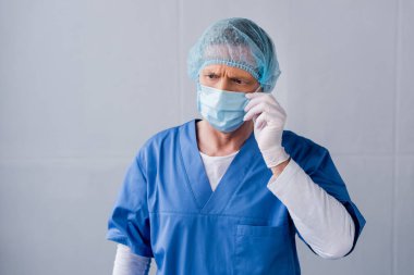 Olgun doktor mavi tıbbi maskeye dokunuyor.