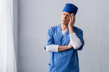 Mavi önlüklü, yorgun ve orta yaşlı doktor gri şapkalı. 