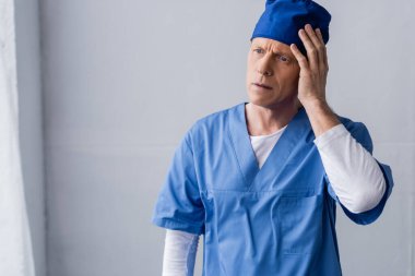 Yorgun ve orta yaşlı doktor mavi önlüklü, gri şapkalı. 