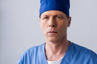 Mavi önlüklü orta yaşlı doktor gri şapkalı.