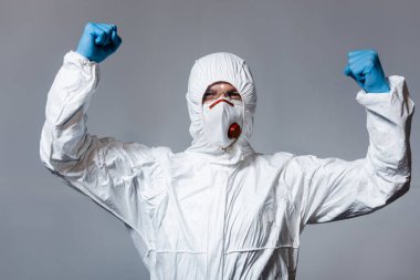 Tehlikeli madde giysisi, tıbbi maske ve gözlük takan olgun bir adam gri renkli yumruklarıyla ayakta duruyor. 