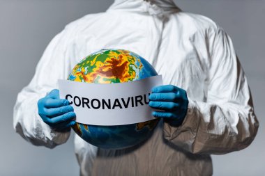cropped view of man in hazmat suit holding globe and paper with coronavirus lettering isolated on grey  clipart