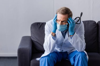 Kanepede otururken steteskop tutan yorgun, olgun bir doktor. 
