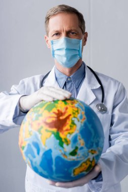 Yetişkin doktorların seçici odak noktası lateks eldivenler ve gri kürenin üzerindeki tıbbi maske. 