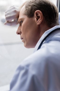 Klinikte pencerenin yanında duran yorgun orta yaşlı doktorun seçici odak noktası 