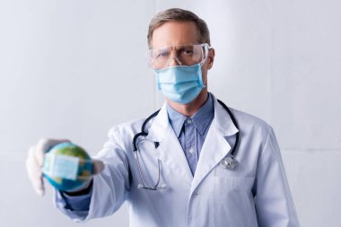 Yetişkin doktorların seçici odak noktası lateks eldiven ve tıbbi maske içinde gri üzerinde küçük bir küre tutması.