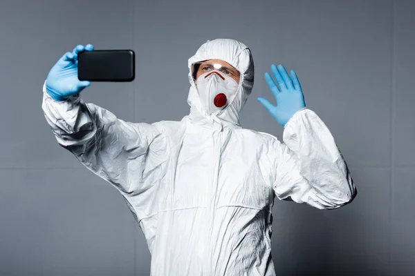 Man Personlig Skyddsutrustning Tar Selfie Och Viftar Med Handen Grå — Stockfoto