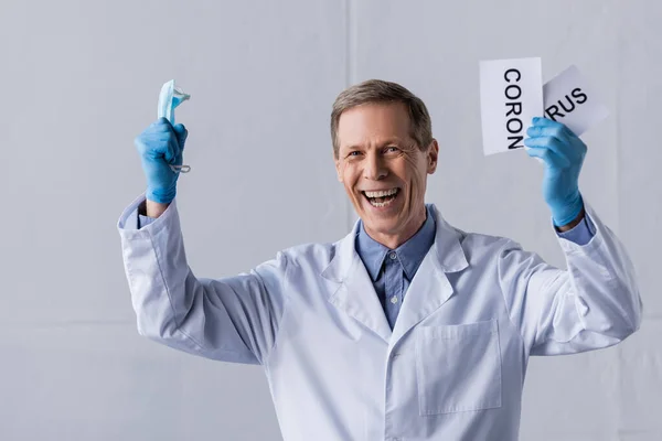 Happy Mature Doctor Holding Medical Mask Ripped Paper Coronavirus Lettering — Stock Photo, Image