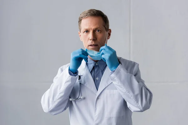 Shocked Mature Doctor Latex Gloves Touching Medical Mask Grey — Stock Photo, Image
