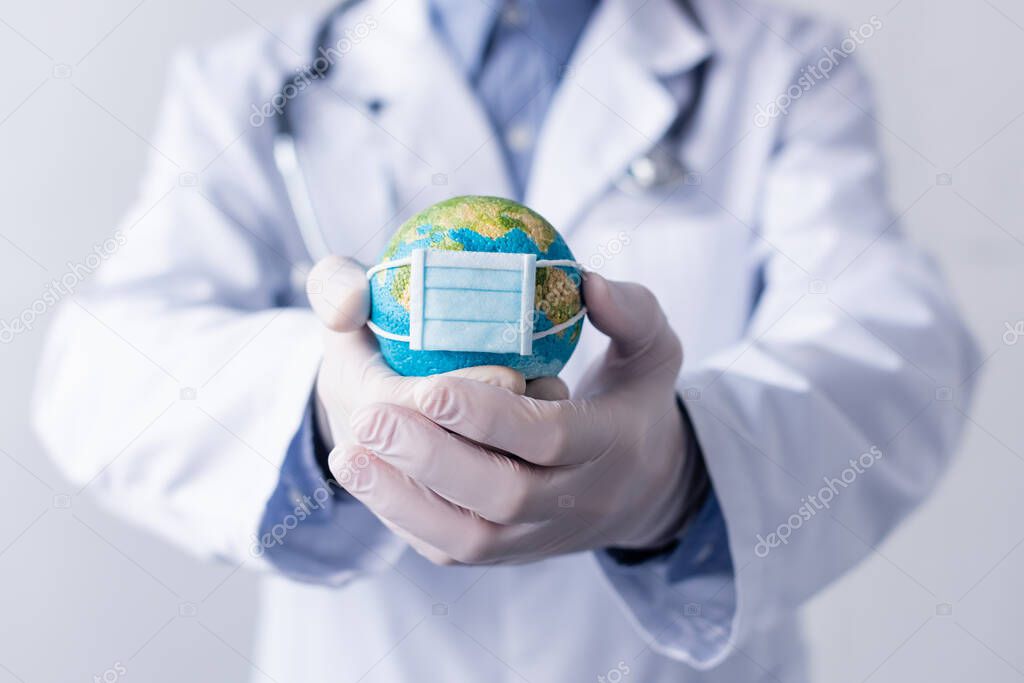 cropped view of middle aged doctor in latex gloves and white coat holding small globe in medical mask isolated on grey