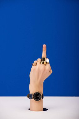 Elinde kol saati olan, mavi üzerinde izole edilmiş orta parmağı olan kadın görüntüsü.