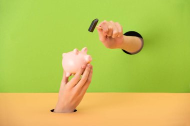 cropped view of woman holding small hammer near pink piggy bank on green and orange  clipart
