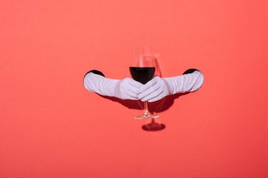 Kırmızıda kırmızı şarap bardağı tutan eldivenli kadın görüntüsü