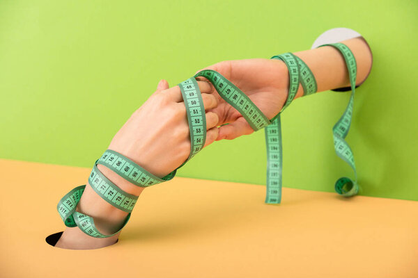 cropped view of woman with measuring tape and clenched hands on green and orange