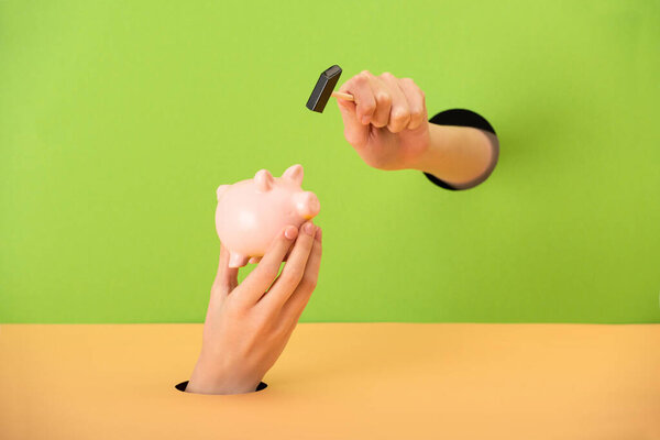 cropped view of woman holding small hammer near pink piggy bank on green and orange 