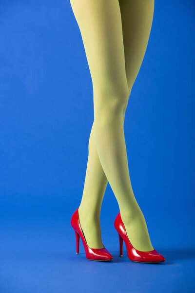 обрезанный вид модели в зеленых колготках и красных каблуках, стоящих на синем
 