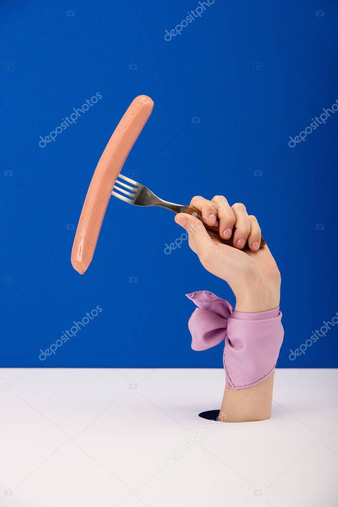 cropped view of woman with ribbon on hand holding fork with tasty sausage isolated on blue