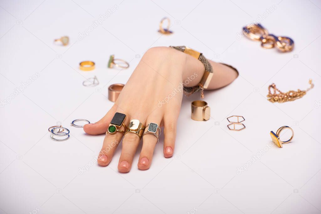 cropped view of woman with bracelet on hand near golden rings on white 