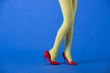 cropped view of stylish model in green tights and red heels posing on blue  clipart