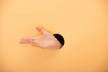 cropped view of hole with hand and woman gesturing on pastel orange  clipart
