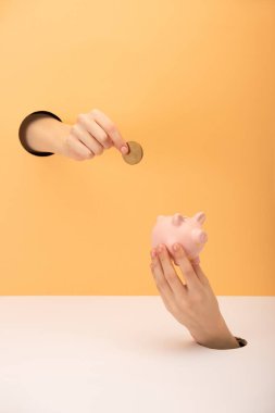 cropped view of woman holding piggy bank and coin on orange and white  clipart
