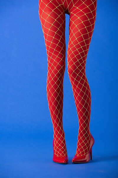 обрезанный вид женщины в рыбных колготках и на красных каблуках, стоящей на синем
 