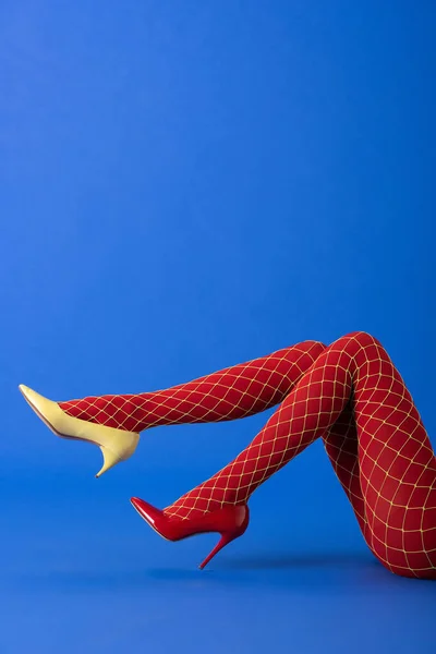 穿着鱼网紧身衣的女人的剪影 黄色和红色高跟鞋躺在蓝色上 — 图库照片