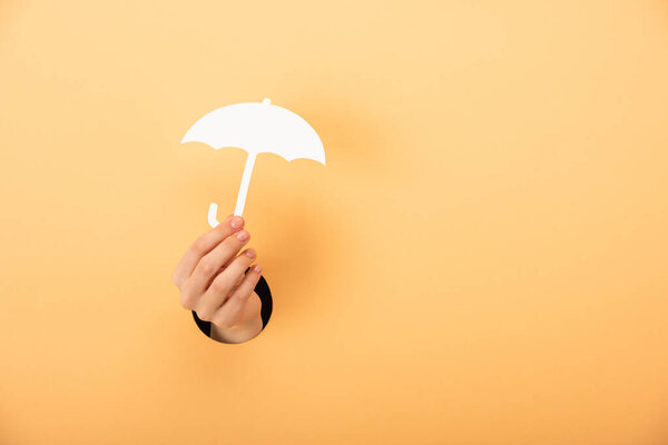cropped view of woman holding paper umbrella on orange