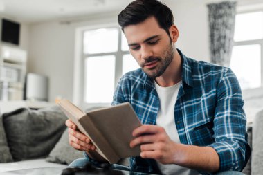 Evde oturup kitap okuyan yakışıklı bir adamın seçici odak noktası.