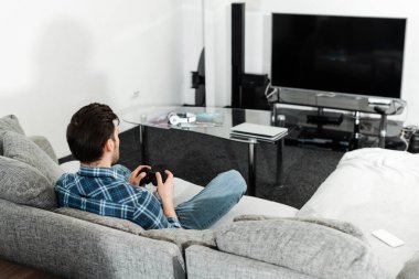 KYIV, UKRAINE - 13 Nisan 2020: Oturma odasındaki kahve masasında bilgisayarın yanında joystick ve kulaklık tutan bir adamın arka görüntüsü 