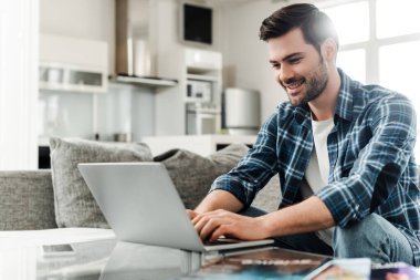Dergi ve akıllı telefonun yanındaki sehpada dizüstü bilgisayar kullanarak gülümseyen serbest yazarların seçici odağı 
