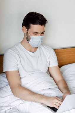 Yatak odasında dizüstü bilgisayarla çalışan maskeli bir serbest çalışan.