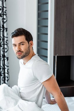 Side view of handsome man looking at camera while sitting on bed  clipart