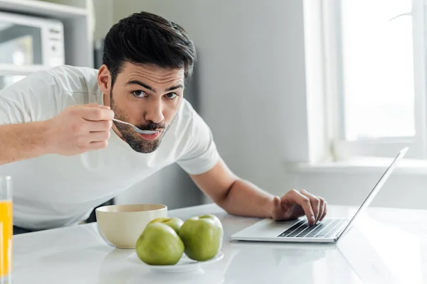 Selective Focus Man Looking Camera While Eating Breakfast Using Laptop — Stock Photo, Image