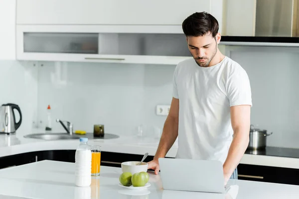 台所のテーブルの上でリンゴ オレンジジュースの近くのノートパソコンを使用して男 — ストック写真