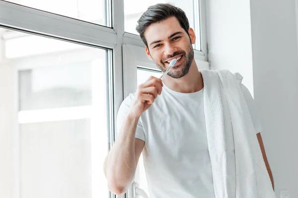 Bonito Homem Sorrindo Para Câmera Enquanto Escova Dentes Perto Janela — Fotografia de Stock