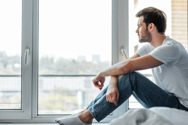 Selective focus of handsome man sitting on windowsill at home 