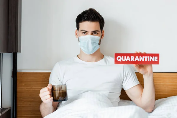 Man Medical Mask Holding Card Quarantine Lettering Cup Coffee Bed — Stock Photo, Image