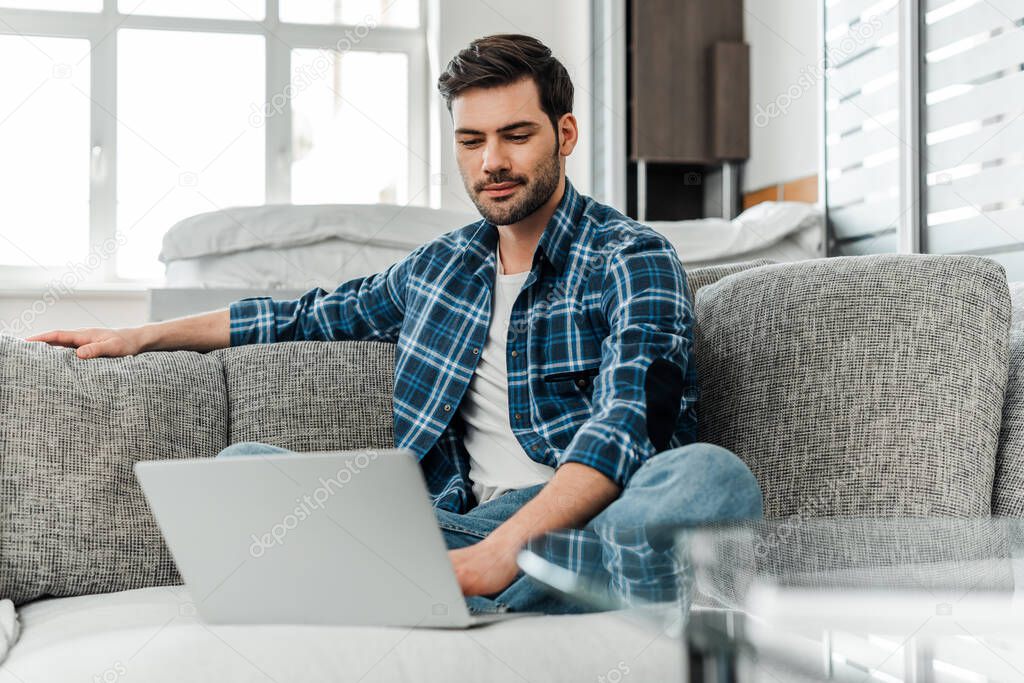 Selective focus of freelancer in plaited shirt working on laptop at home 