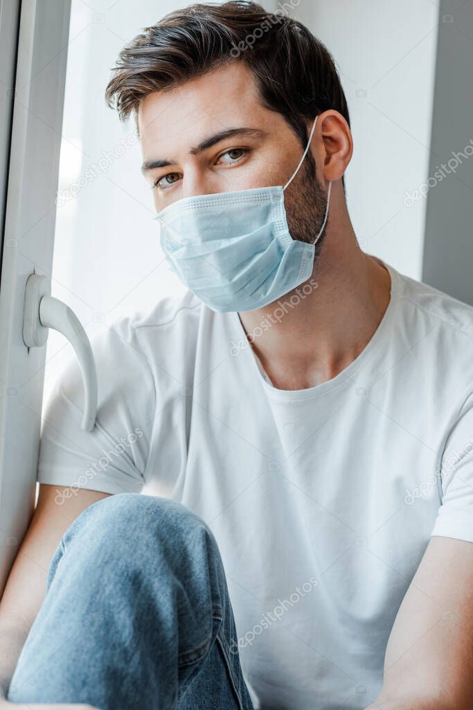 Man in medical mask looking at camera near window 