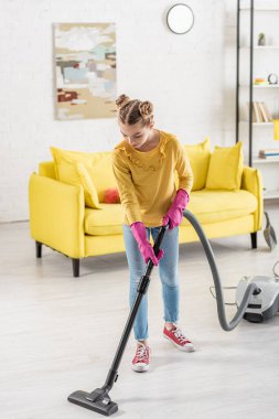 Oturma odasında elektrikli süpürgeyle temizlik yapan sevimli bir çocuk.